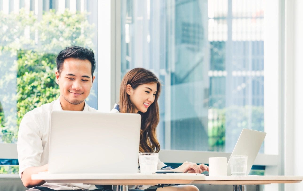 Two people sitting at a table with laptops.