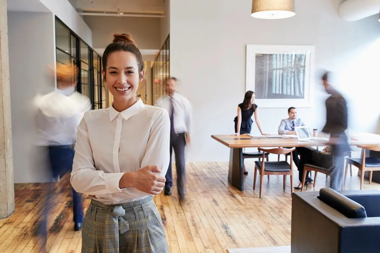 A woman standing in an office with people behind her.